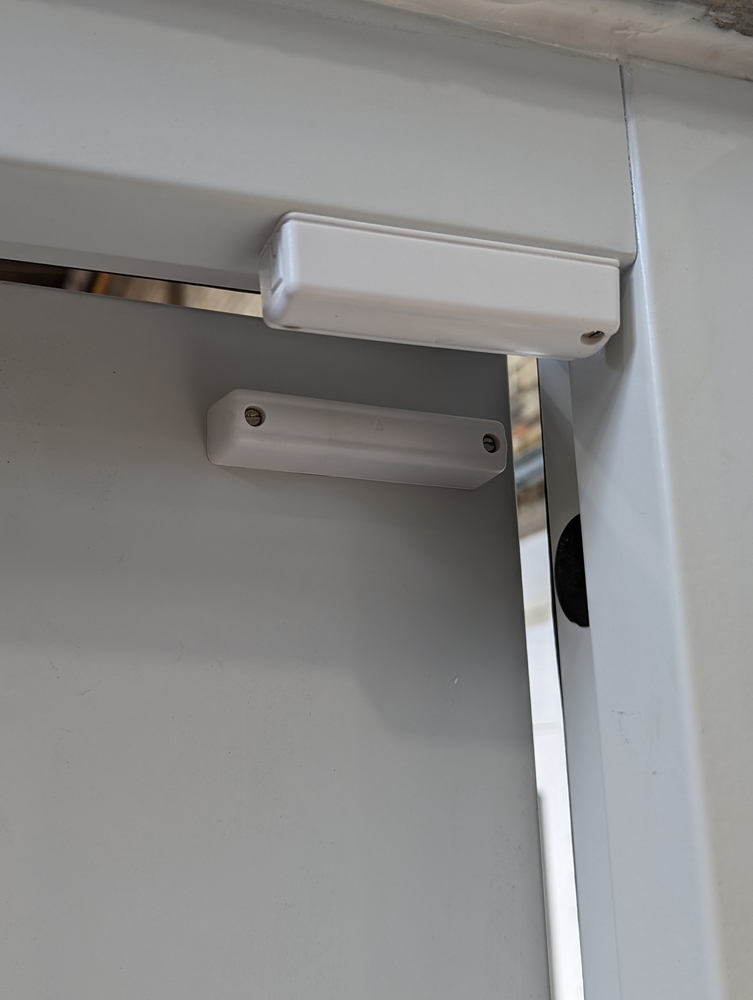 Testing a home alarm system by opening a door to trigger the magnetic contact sensor and verify the signal reaches the monitoring centre