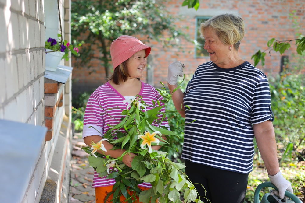 Smiling grandmother and young granddaughter laughing together while holding cut lily flowers in a garden